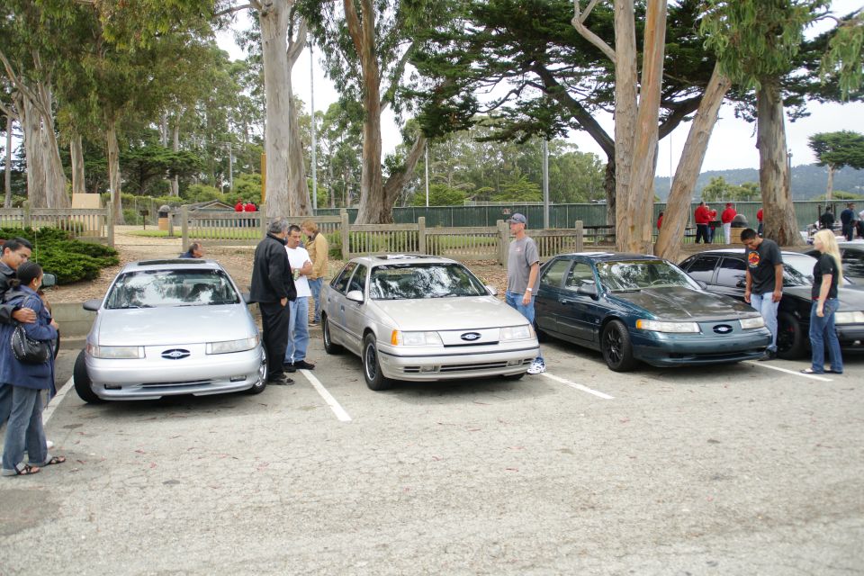 Silver sedan parked in a lot, front view, with people standing nearby