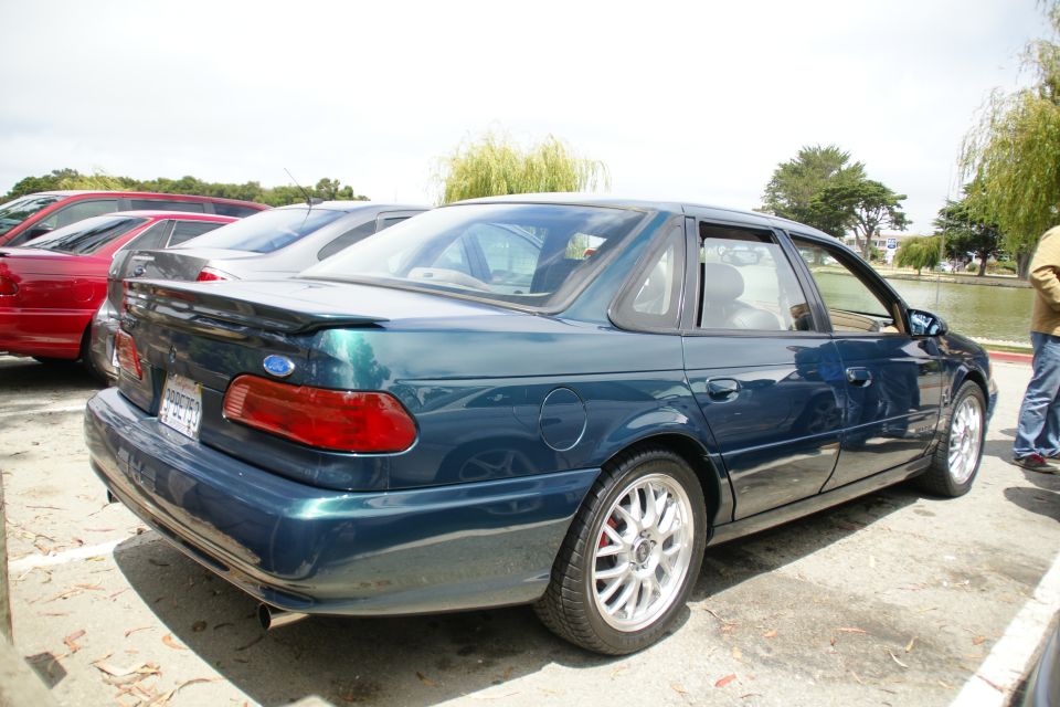 Dark green sedan parked next to a red car, with a lake and trees in the background