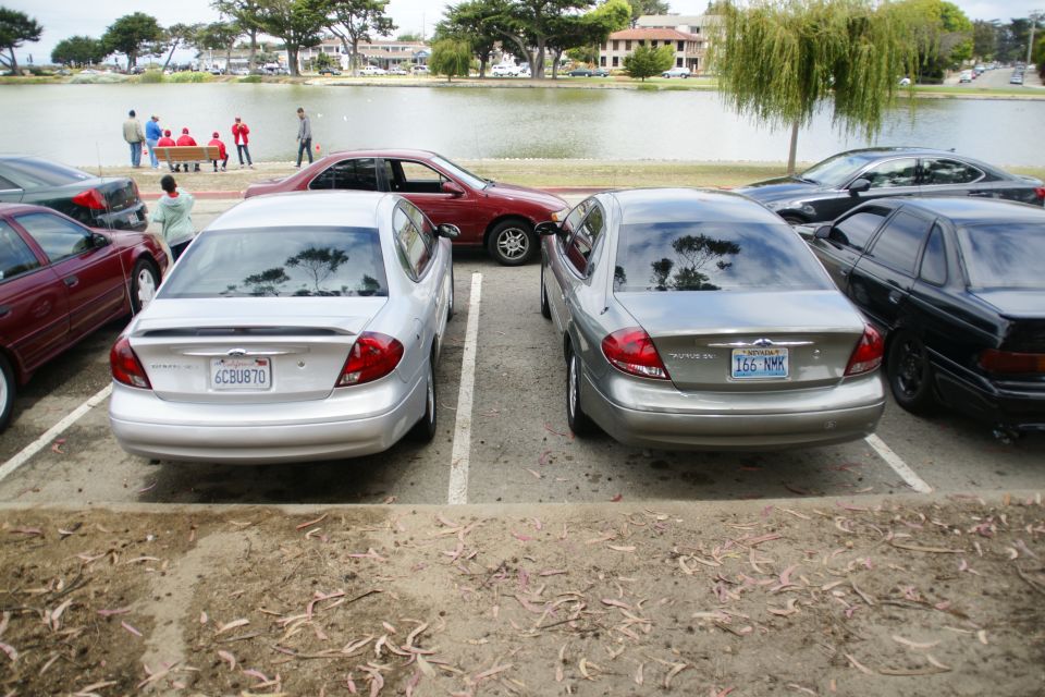 Two Ford Tauruses parked near a lake with people in the background