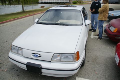 1995 Ford Taurus - White 1995 Ford Taurus parked in a lot with other vehicles and two people standing.