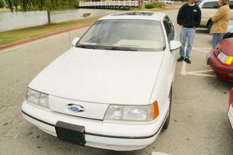 1995 Ford Taurus - Front view of a white 1995 Ford Taurus sedan parked in a lot with a lake in the background.