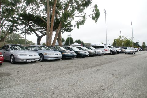 1995 Ford Taurus - Several cars are parked in a lot under a cloudy sky, with trees and tents visible.