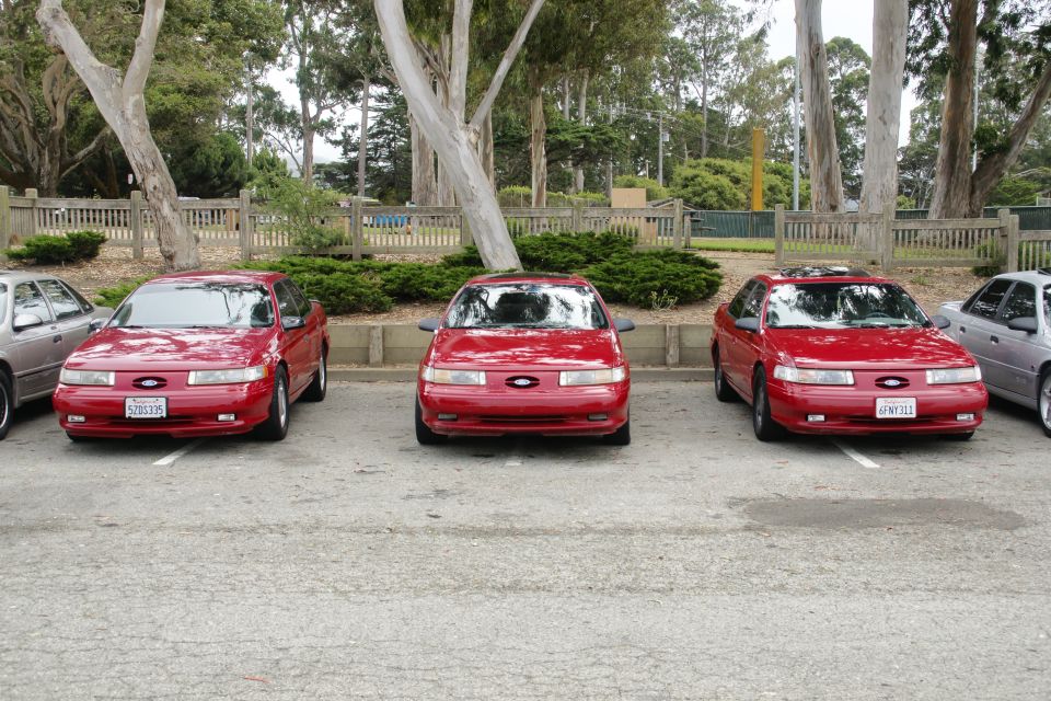 Three red Ford Taurus sedans parked in a lot. The middle one is slightly forward of the other two