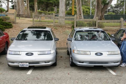 1995 Ford Taurus - Two silver 1995 Ford Taurus sedans are parked next to each other, their front ends.