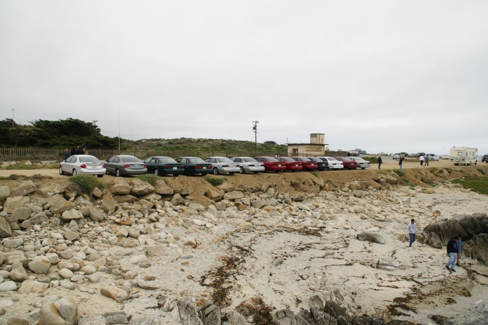 Side view of a line of cars, including a 1995 Ford Taurus, parked along a rocky coastline