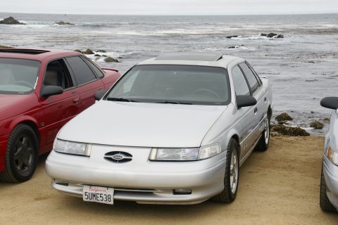 1995 Ford Taurus - Three cars parked on a dirt lot overlooking the ocean, with the front of a silver 1995 Ford Taurus prominent.