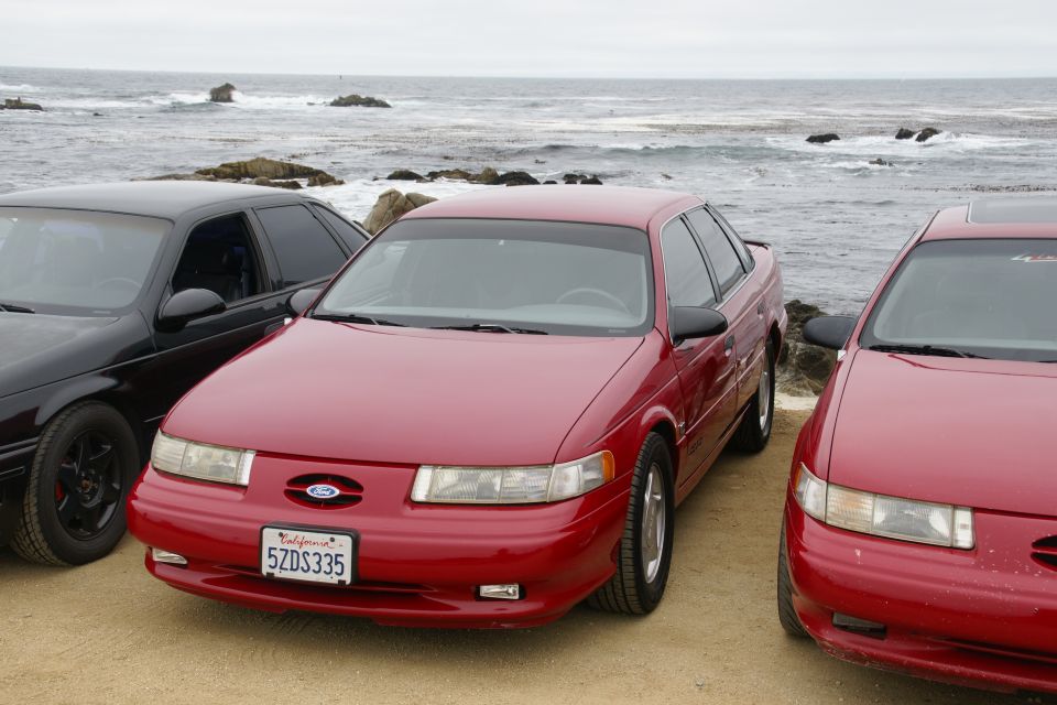 Red sedan with California plates 5ZDS335 parked next to a black sedan and another red sedan by the ocean
