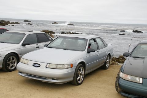 1995 Ford Taurus - Three sedans are parked on a sandy area near the ocean, with waves crashing on rocks.