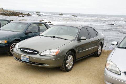 1995 Ford Taurus - A gray Ford Taurus is parked on a dirt lot near the ocean, with other vehicles present.