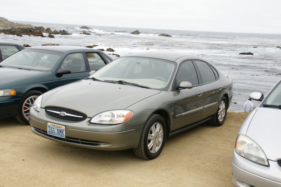 Gray Ford Taurus parked by the ocean, with another car to its left and a silver car to its right