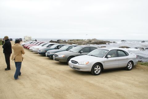 1995 Ford Taurus - A line of sedans, likely from the early 2000s, parked near the coast on a cloudy day.
