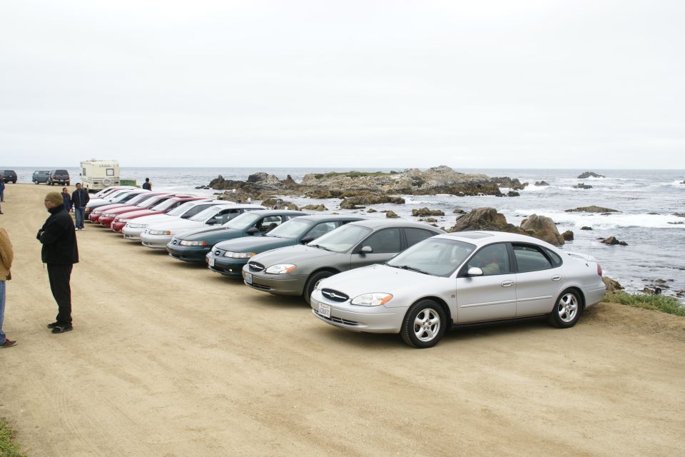 Silver sedan parked on dirt road by the ocean, showing front quarter view