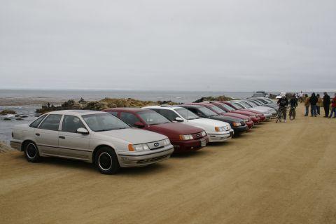 1995 Ford Taurus - A line of sedans parked by the ocean on a cloudy day.