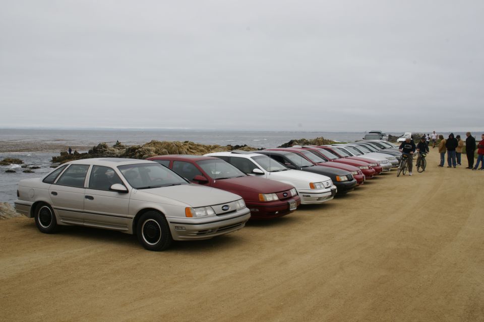 Silver sedan parked on dirt lot near ocean, front 3/4 view