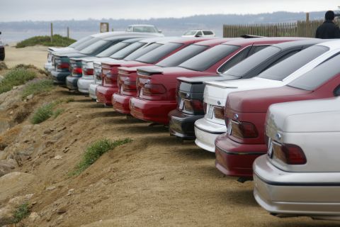 1995 Ford Taurus - Multiple sedans are parked in a line on a dirt lot near the coast.