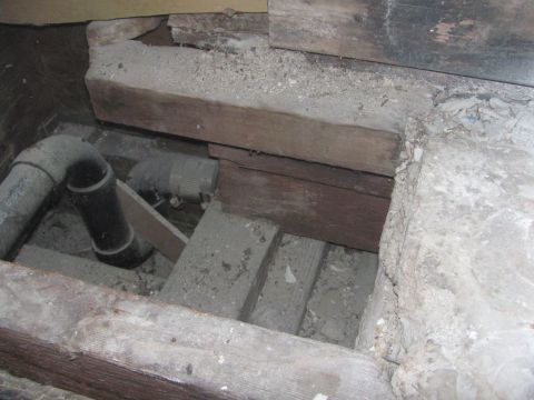 1968 Ford Mustang - A view of plumbing pipes and wooden structural elements beneath the floorboards, showing a dusty and unfinished environment.