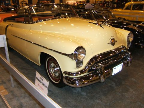 2012 Ford Crown Victoria - A cream 1951 Oldsmobile Super 88 convertible is displayed at an auto show, with other vehicles visible in the background.
