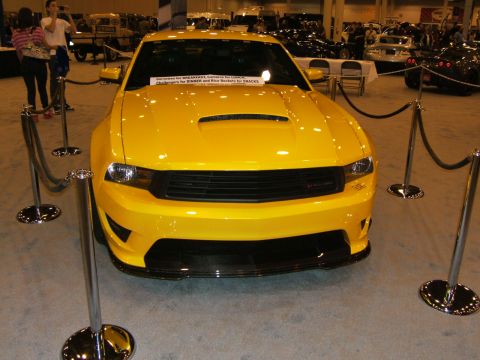 2012 Ford Crown Victoria - A yellow sports car is displayed at an auto show, with stanchions and ropes around it.