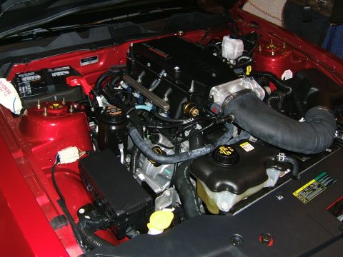 2012 Ford Crown Victoria - The engine bay of a car is shown, a prominent black supercharger and red painted components.