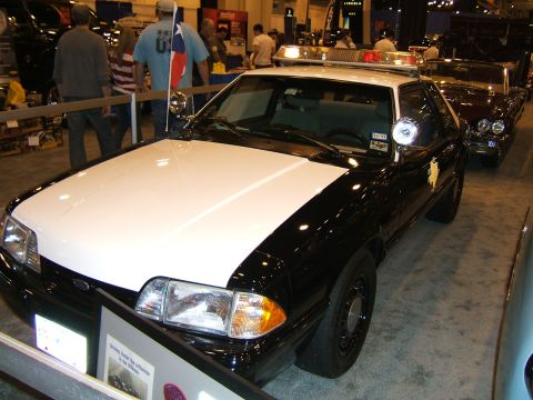 2012 Ford Crown Victoria - This police car, likely a Ford Mustang, is displayed at an auto show. Another vehicle is visible to the right.