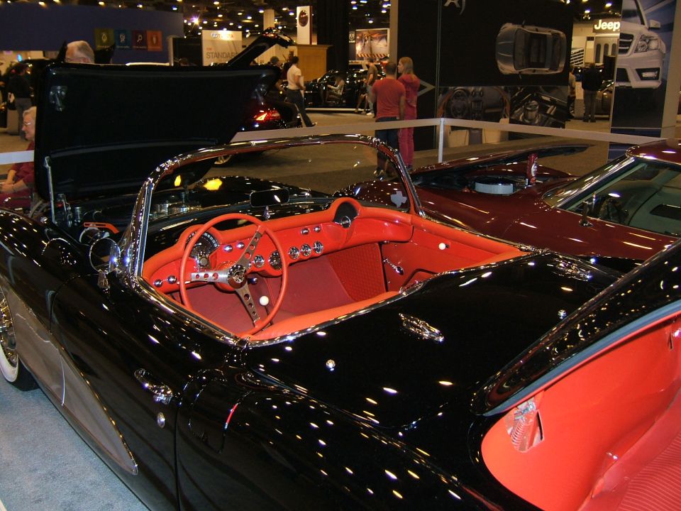 Black 1956 Chevrolet Corvette convertible with red interior, hood open, parked next to a red car