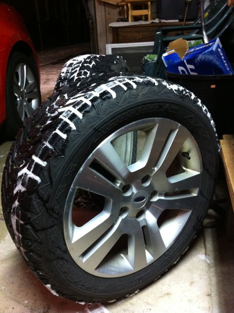 2010 Hyundai Genesis - Winter tire and alloy wheel shown in a garage setting, with a portion of a red vehicle in the background.