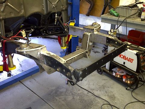 1941 Ford Pickup - Close-up view of a vehicle's frame and suspension components being worked on in a garage, with welding equipment visible.