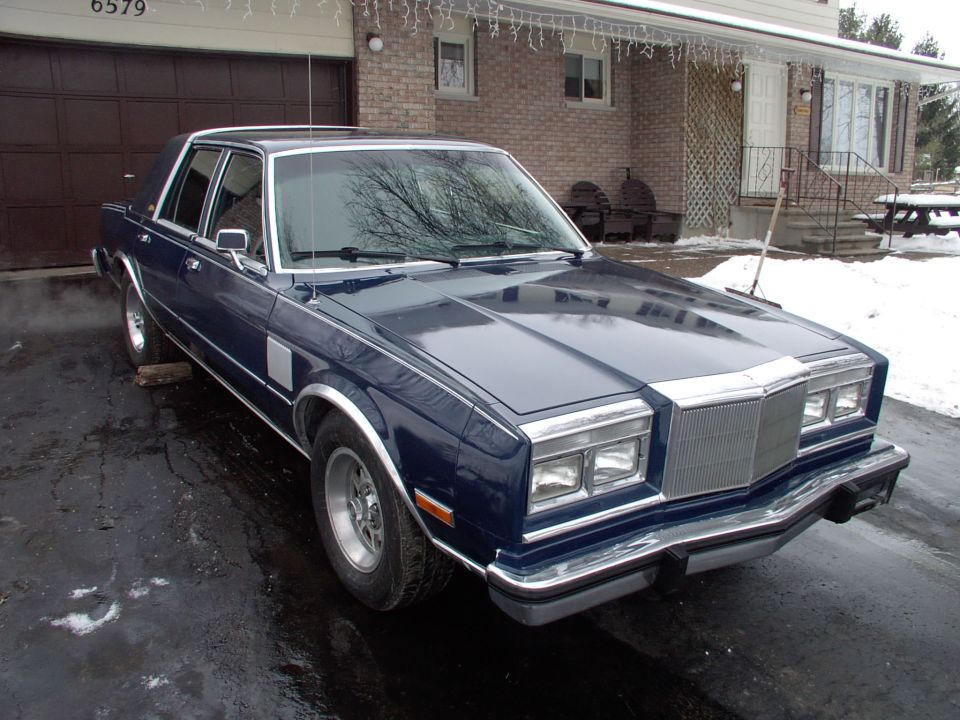 Dark blue Chrysler Fifth Avenue sedan on a snowy driveway, front three-quarter view