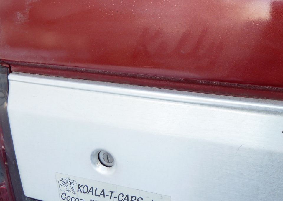 Close-up of a red vehicle's rear quarter panel with a silver trim piece and a Koala-T-Caps sticker