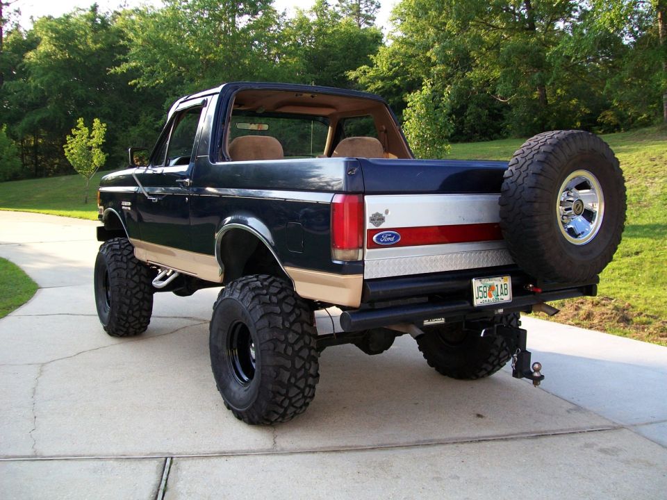Dark blue and tan Ford Bronco with lifted suspension and large off-road tires, spare tire mounted on rear