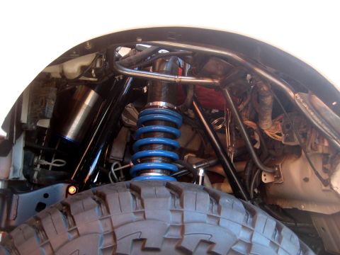 1996 Ford Bronco - Inside the front wheel well of a lifted truck, showing a long-travel coilover shock with a blue spring and threaded body mounted to a tubul…
