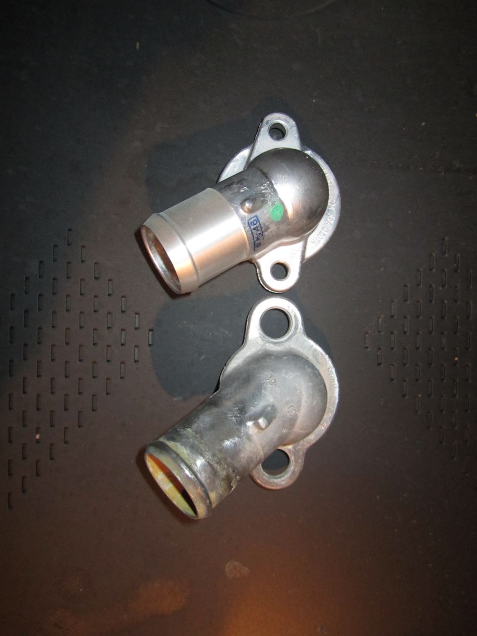 Two metal water neck housings, one silver and one darker, on a black surface