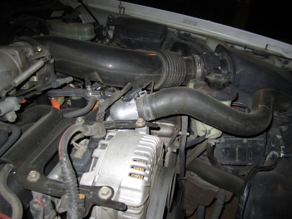 Engine bay with alternator, air intake hose, and coolant hoses visible