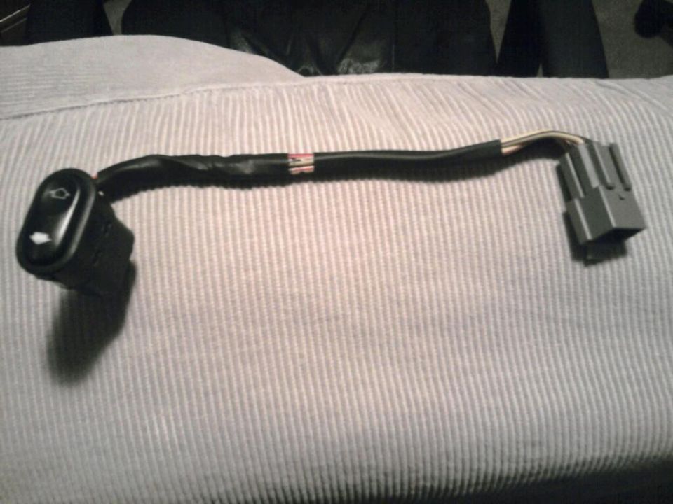 Car door switch with a wiring harness attached, resting on a textured surface