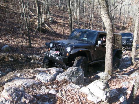 2007 Jeep Wrangler - Two Jeeps tackle a challenging, rocky path through a forest during daylight.
