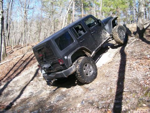 2007 Jeep Wrangler - A black Jeep Wrangler navigates a steep, rocky incline on a wooded trail.