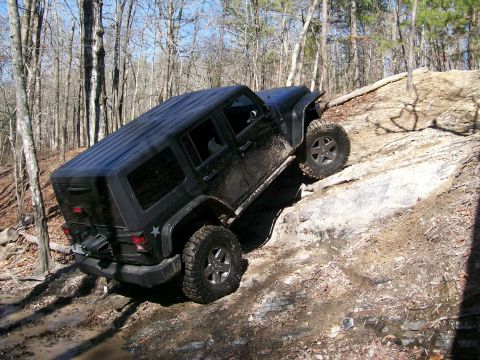 2007 Jeep Wrangler - A black 2007 Jeep Wrangler navigates a challenging rocky trail in a wooded area.