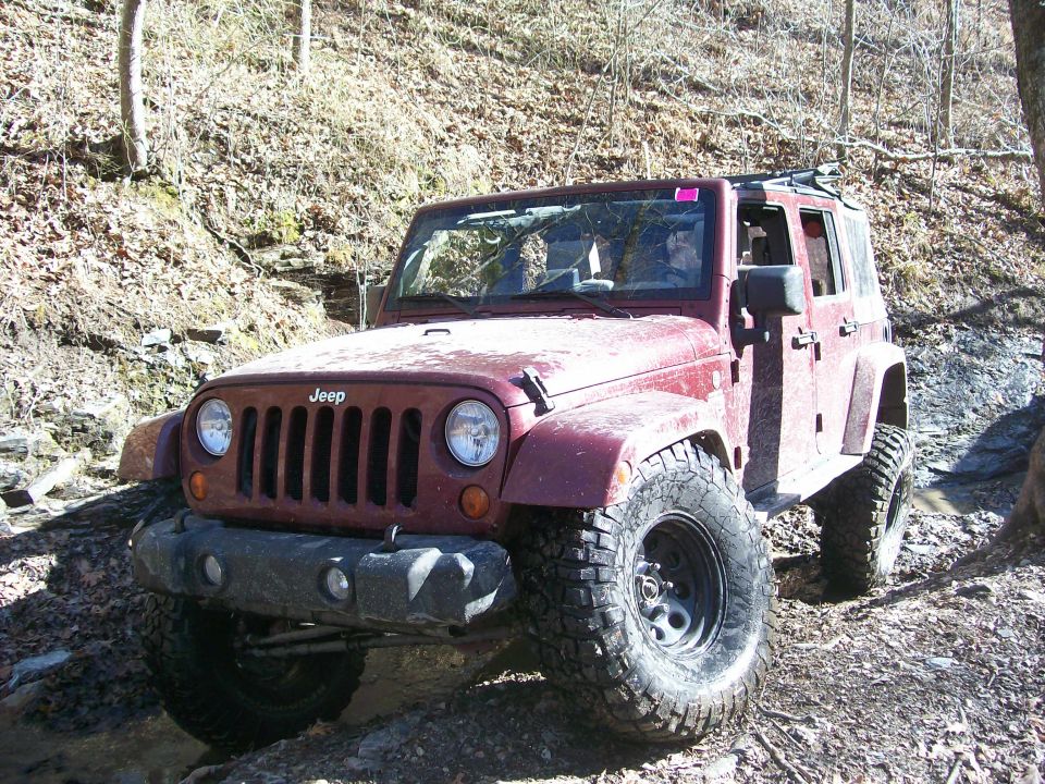 Red 2007 Jeep Wrangler on a rocky trail, front 3/4 view