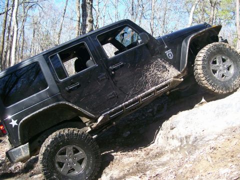 2007 Jeep Wrangler - Black Jeep Wrangler navigating a challenging off-road trail with mud and rocks.