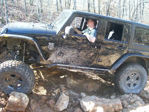 2007 Jeep Wrangler - A black Jeep Wrangler navigates a rocky trail, its tires kicking up mud.