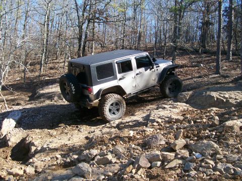 2007 Jeep Wrangler - A silver 2007 Jeep Wrangler tackles a challenging rocky terrain in a wooded area.