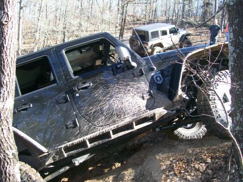2007 Jeep Wrangler - A black Jeep Wrangler, mud-splattered and equipped with off-road gear, navigates a trail with another Jeep visible in the background.