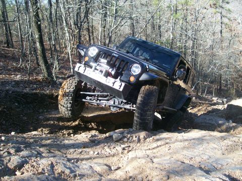 2007 Jeep Wrangler - A black Jeep Wrangler navigates a rocky off-road trail in a wooded area.