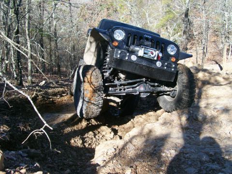 2007 Jeep Wrangler - A black 2007 Jeep Wrangler navigates a challenging off-road trail with its front tire elevated.