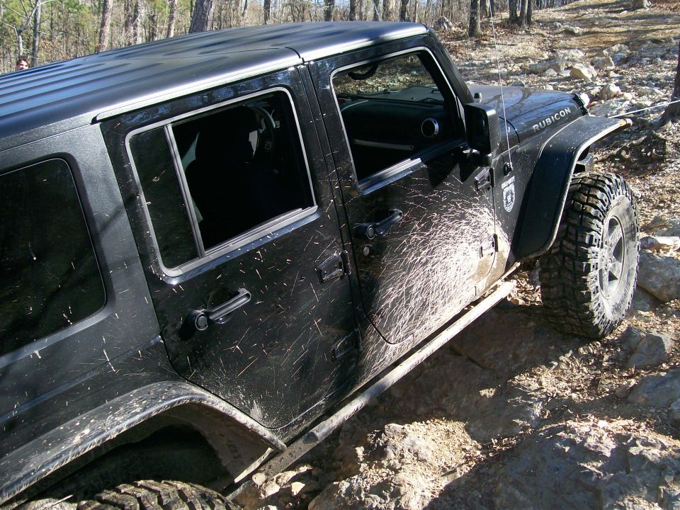 Black 2007 Jeep Wrangler Rubicon with mud splatters on the side, driving over rocks