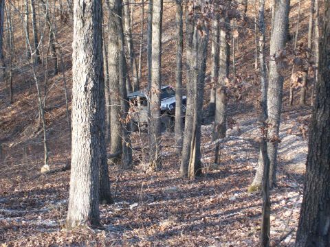 2007 Jeep Wrangler - A Jeep Wrangler navigates a wooded trail during daylight, with the ground covered in fallen leaves.