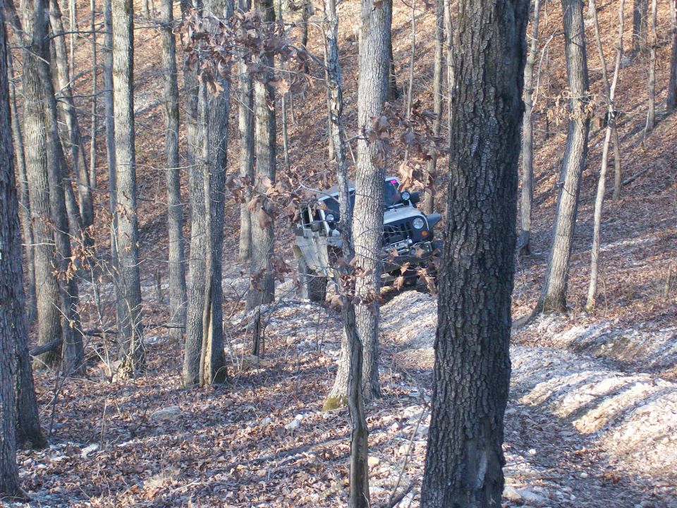 White 2007 Jeep Wrangler on a wooded trail, angled up a slope