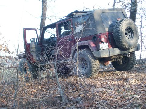 2007 Jeep Wrangler - A red 2007 Jeep Wrangler navigates an off-road trail, showing its capabilities with large tires and a soft top.