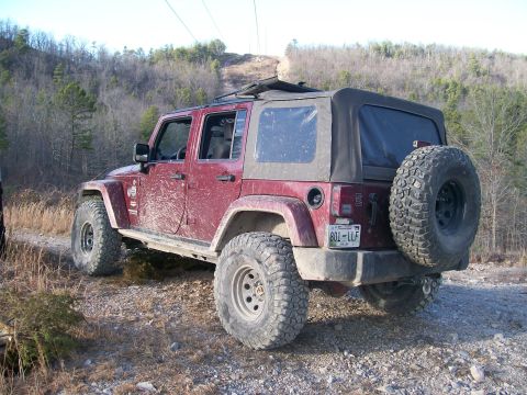 2007 Jeep Wrangler - Red 2007 Jeep Wrangler parked on a dirt road with trees in the background.