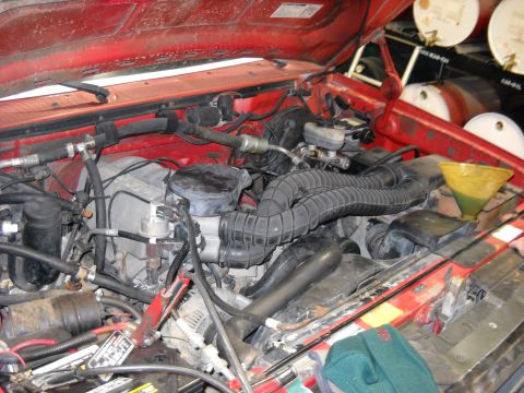 1993 Ford C-150 (Centurion Conversions) - Engine bay of a red Ford F-150, showing the engine and various hoses and components.